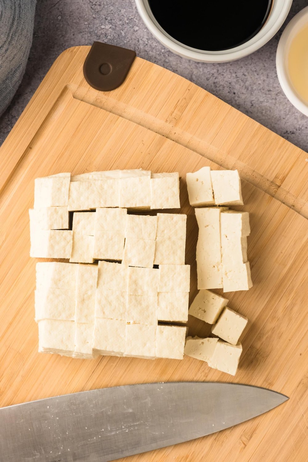 Tofu cut into pieces on a cutting board.