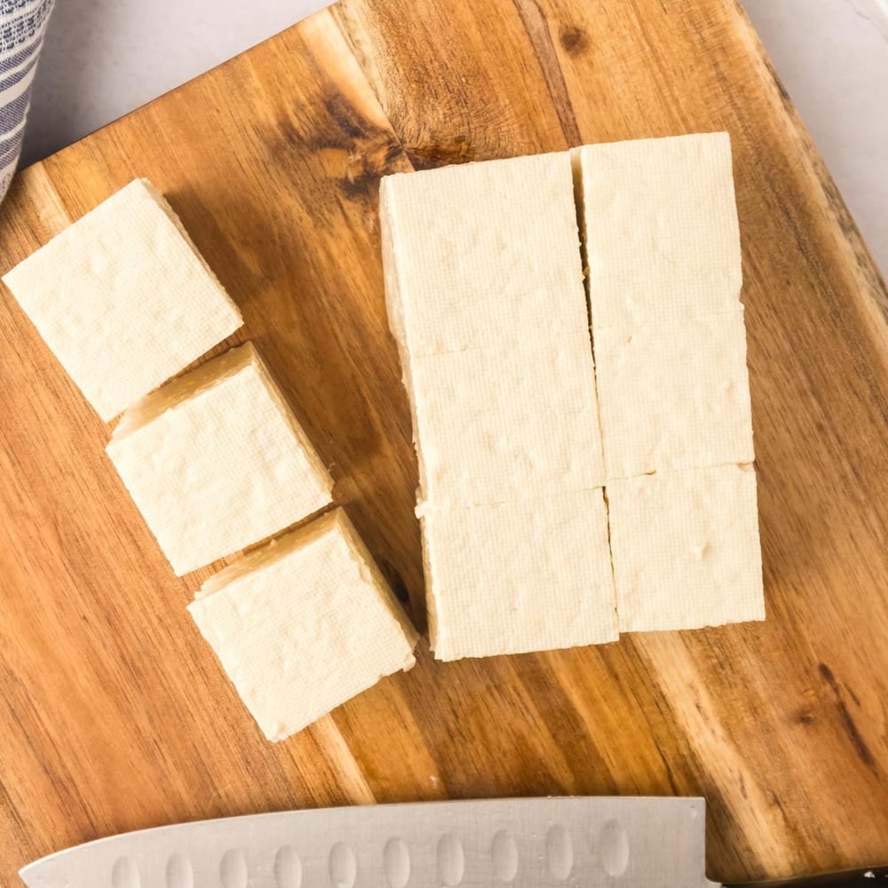 Tofu on a cutting board, chopped.