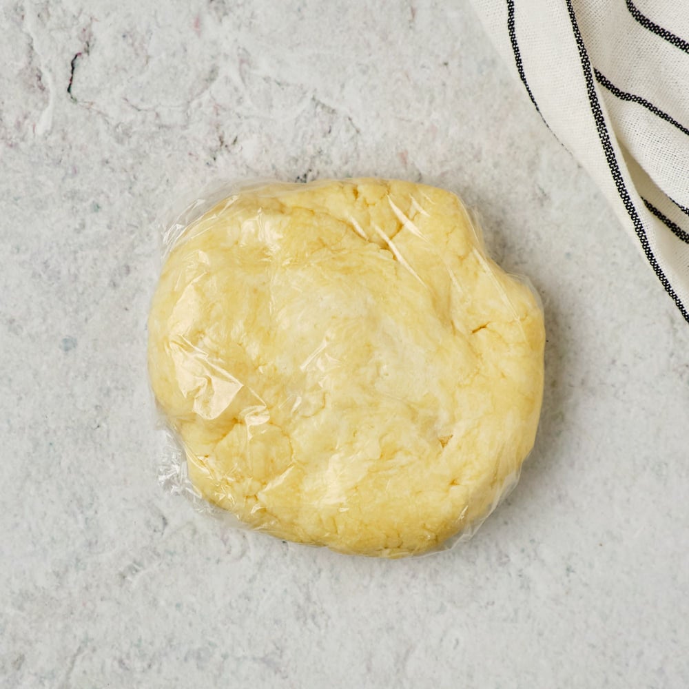 Vegan shortcrust dough wrapped in plastic wrap.