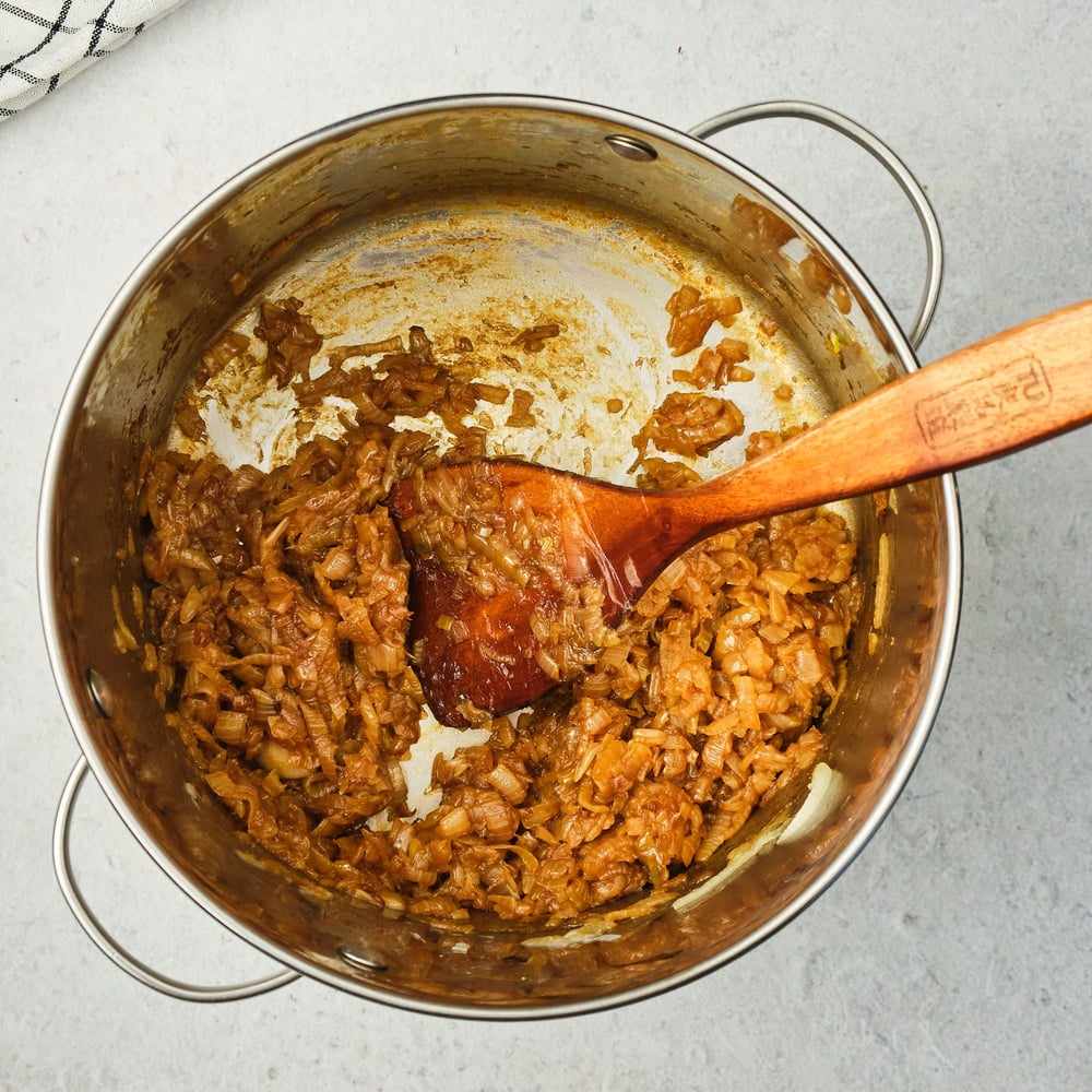 Onions in a large pot with a wooden spoon after being caramelized.