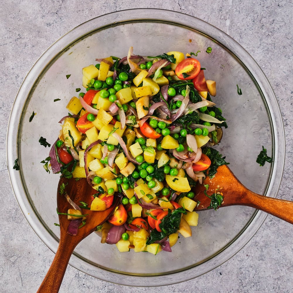 Veggies combined in a large mixing bowl with two wooden spoons.