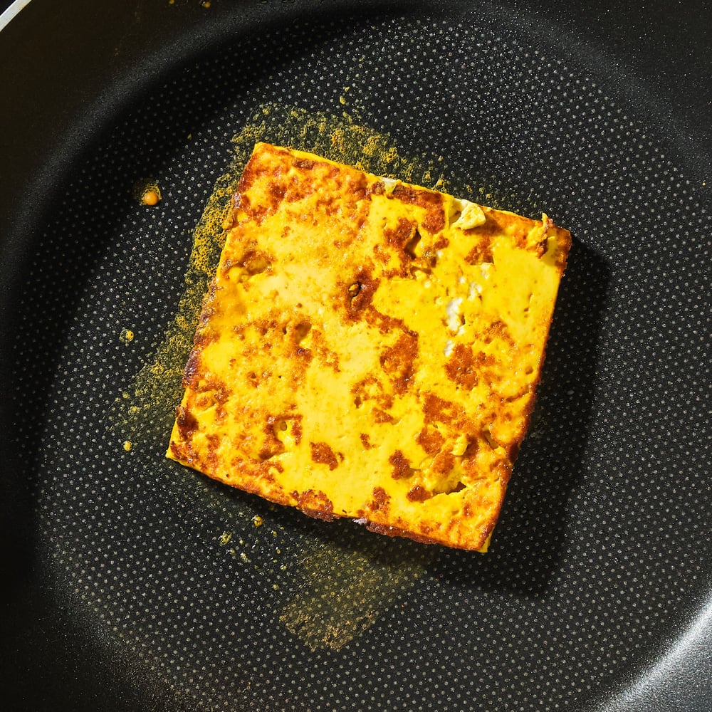 A slice of seasoned tofu in a pan after flipping.