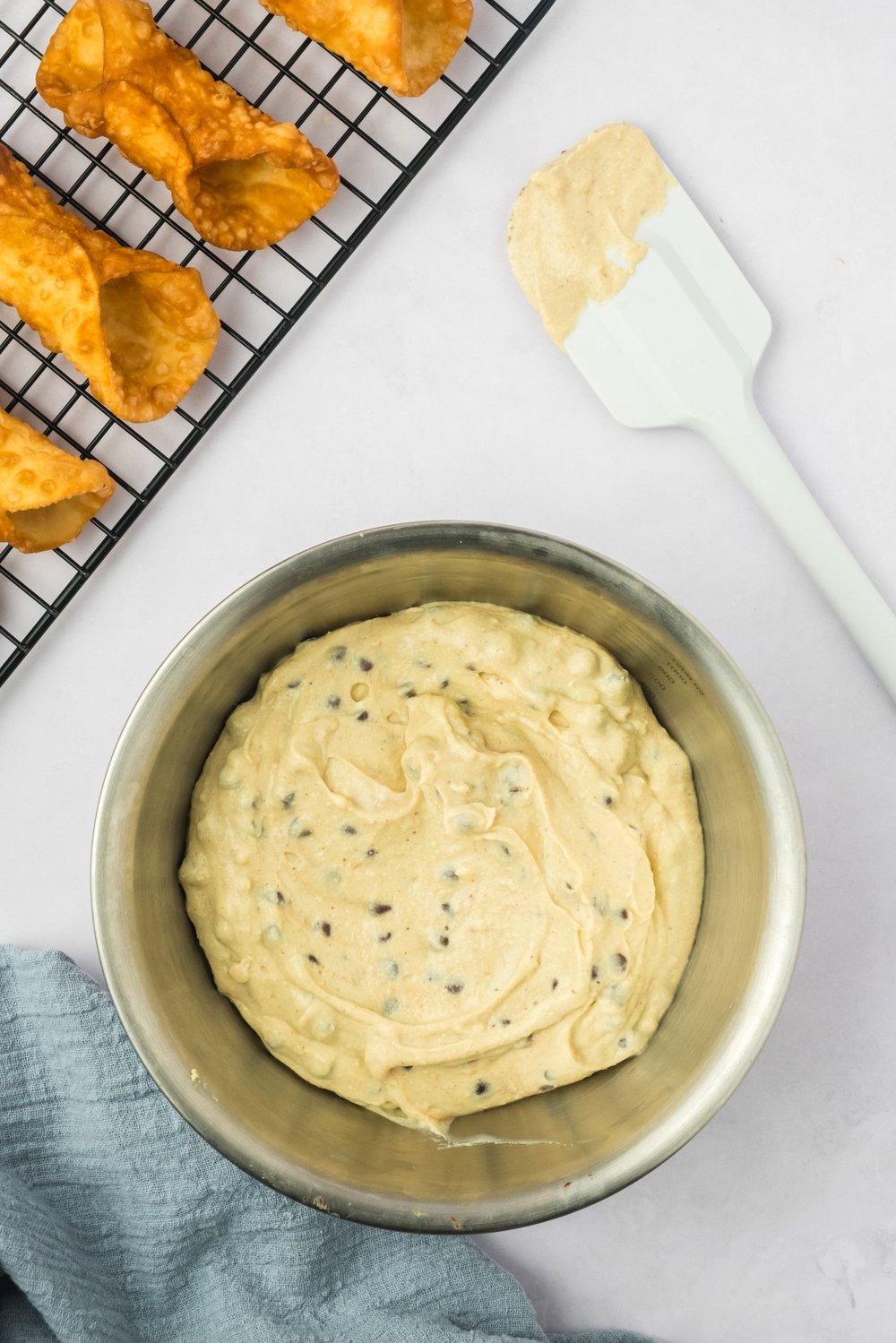 A bowl of finished tofu ricotta filling next to a wire rack of cannoli shells.