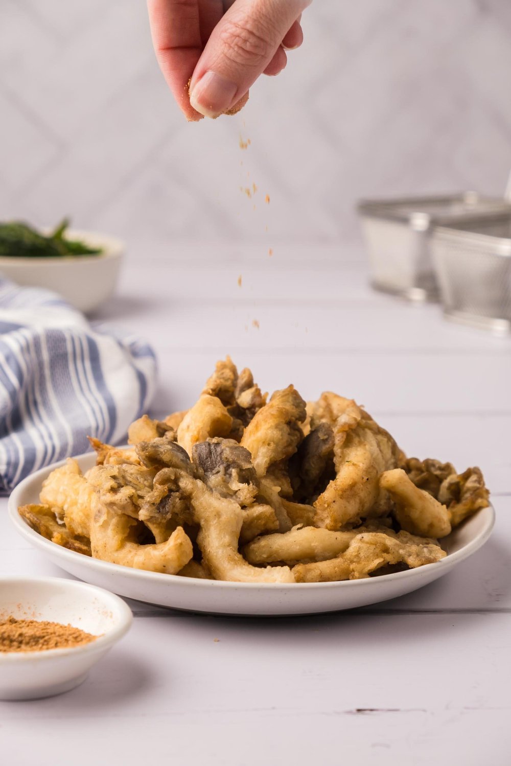 Sprinkling seasoning powder on a plate of fried oyster mushrooms.