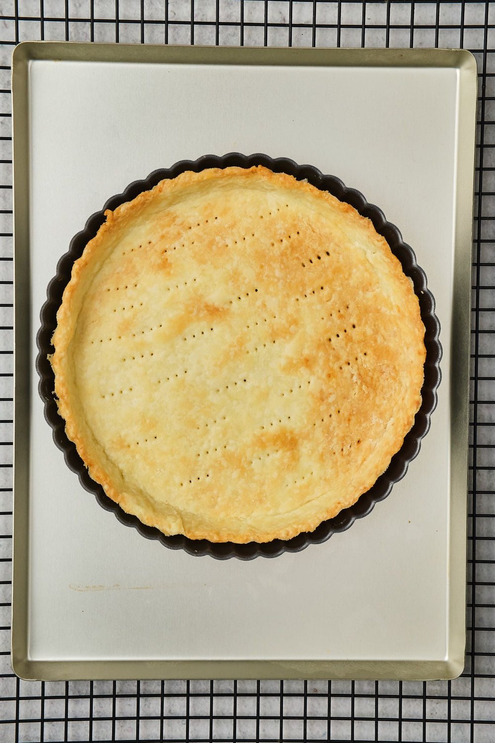 A baked shortcrust cooling in a tart pan on a baking sheet on a wire rack.