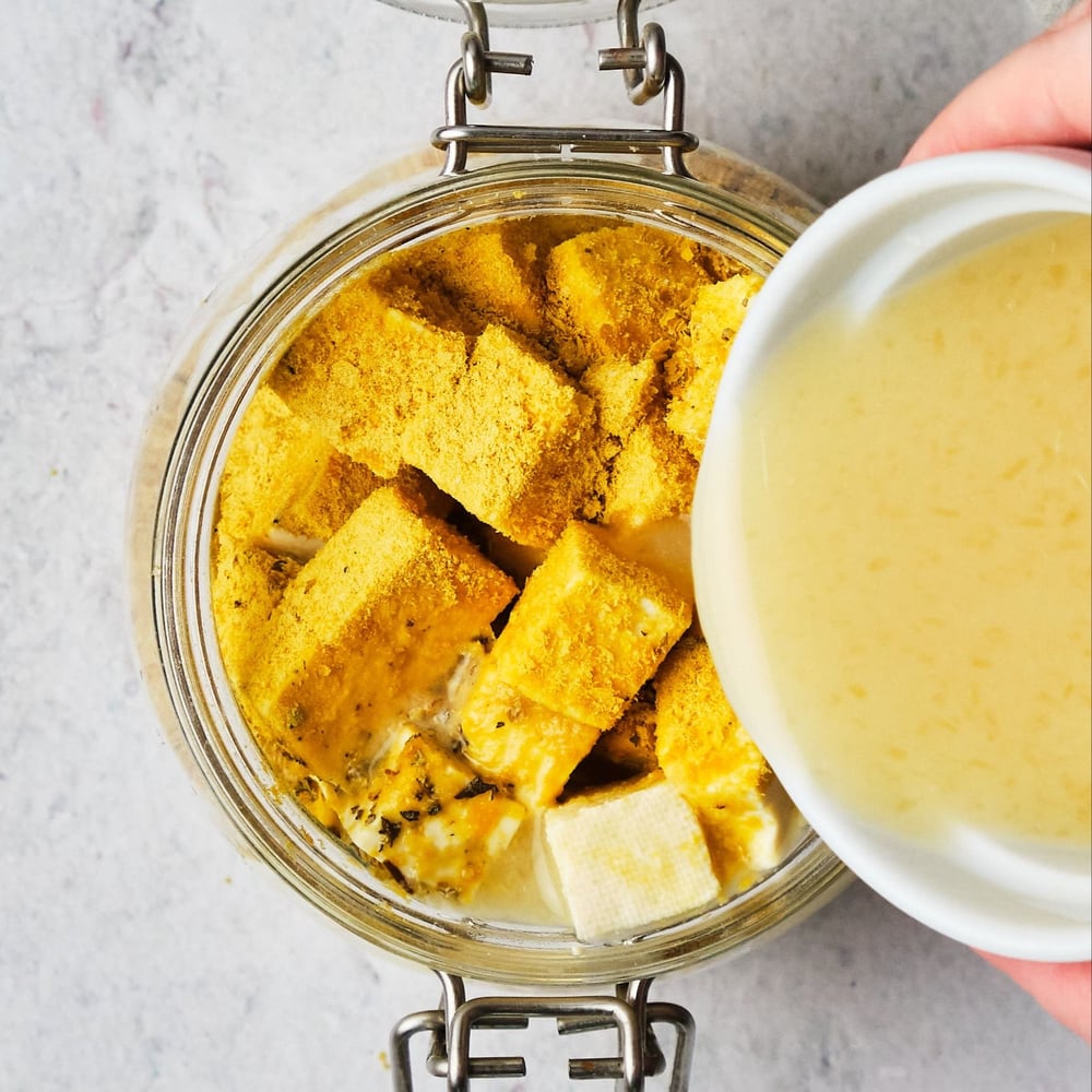 A hand pouring liquid over tofu coated in seasonings.