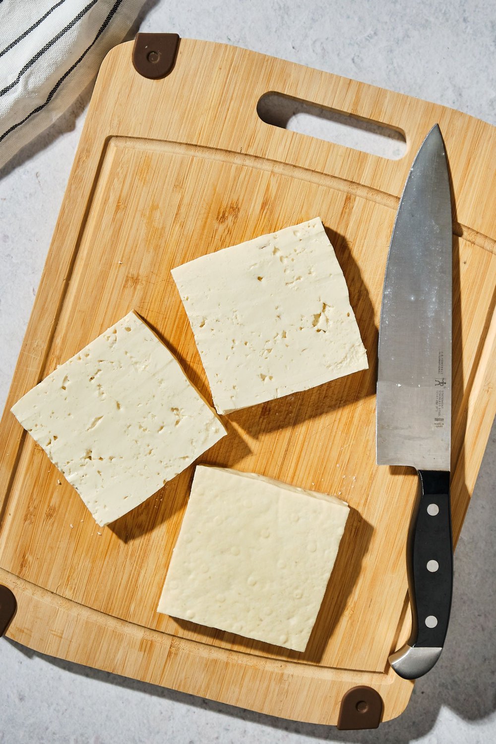 A block of tofu sliced into three pieces on a cutting board next to a knife.