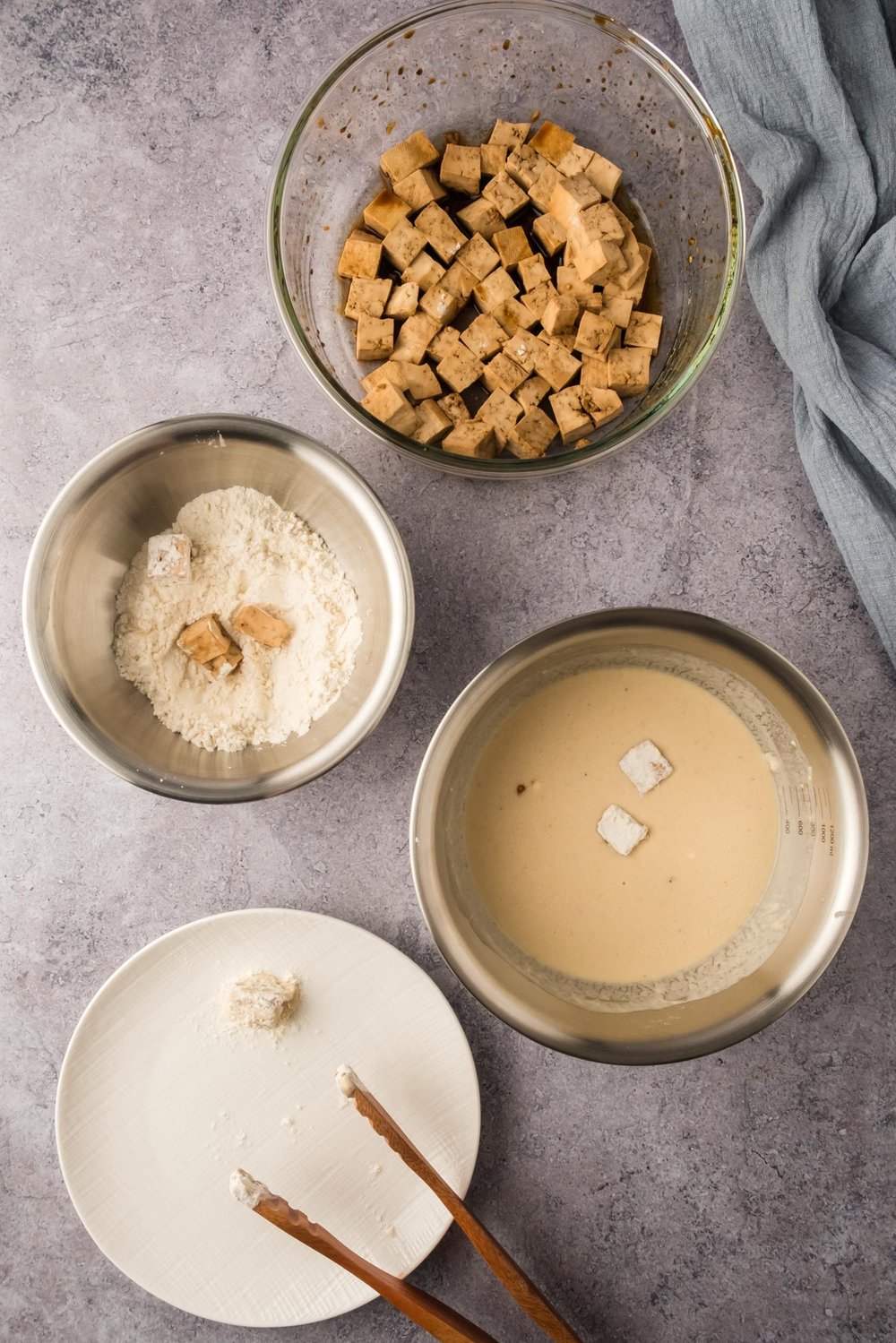 Marinated pieces of tofu being coated in batter, then flour, then placed on a plate.