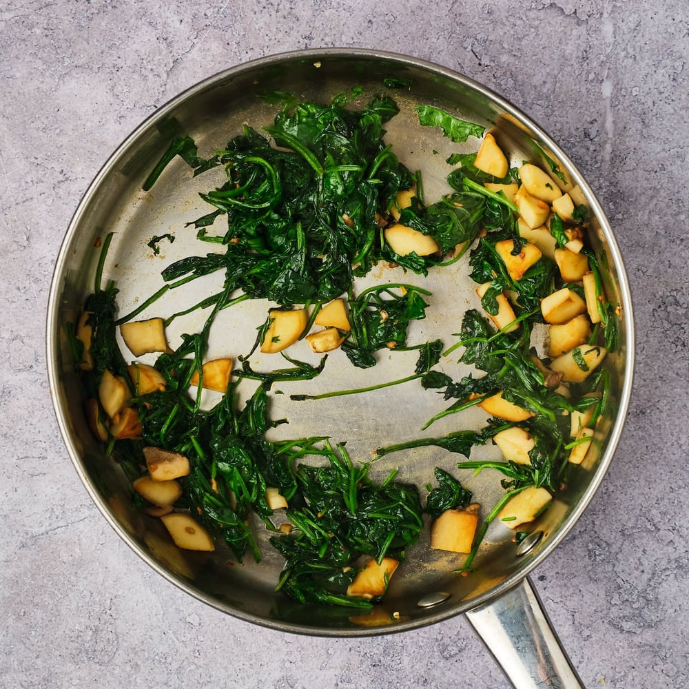 Mushrooms, garlic, and spinach in a saute pan after being cooked.