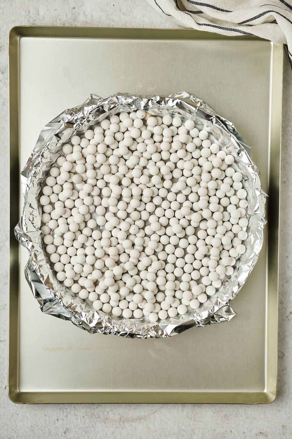 A tart pan with a shortcrust covered with foil and pie weights, placed on a metal baking sheet.