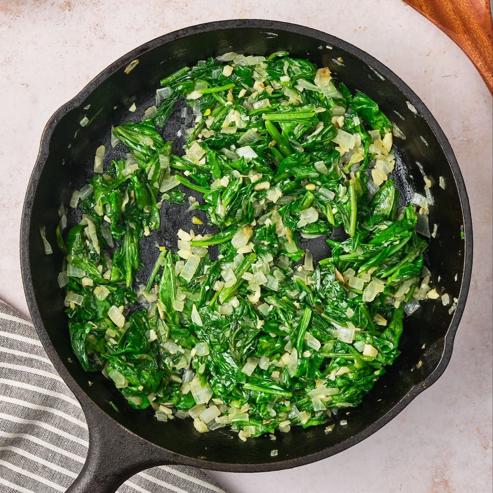 Wilted spinach in a pan with garlic and onions.