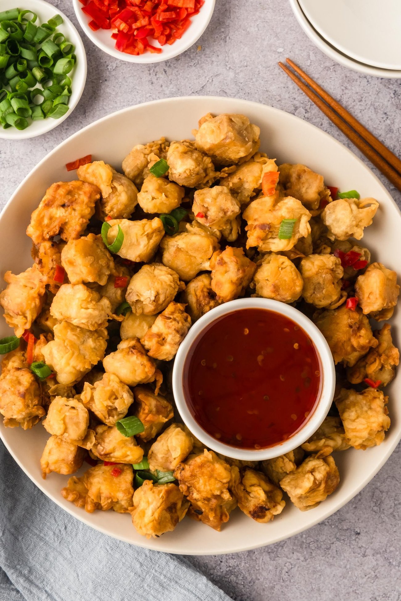 A big bowl of crispy fried tofu on a table with a ramekin of sweet chili sauce.