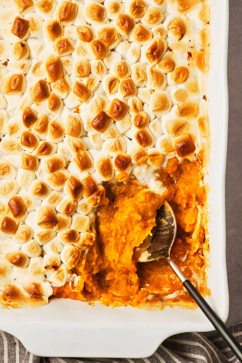 A top-down view of a vegan sweet potato casserole topped with marshmallows, with a serving spoon in the corner of the dish.
